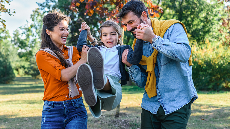 Happy parents and their daughter enjoying autumn in the park.