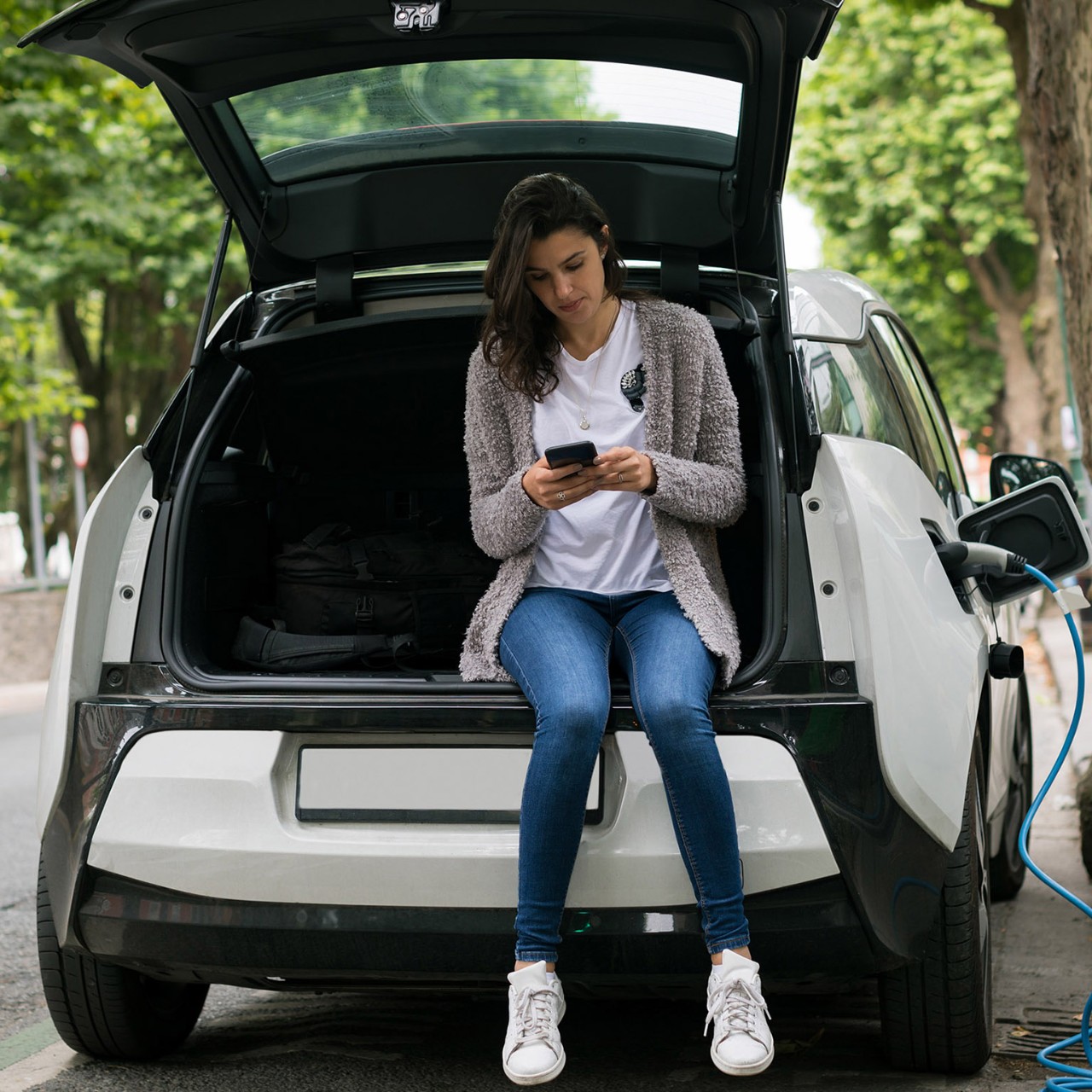 Woman using mobile phone while charging electric car at charging station