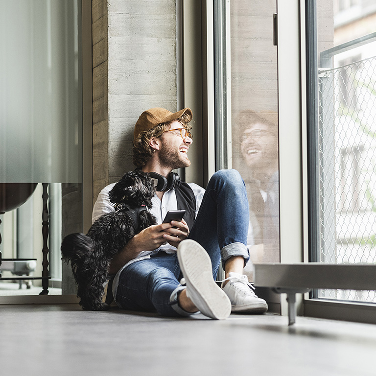 Laughing casual young man sitting at the window with dog
